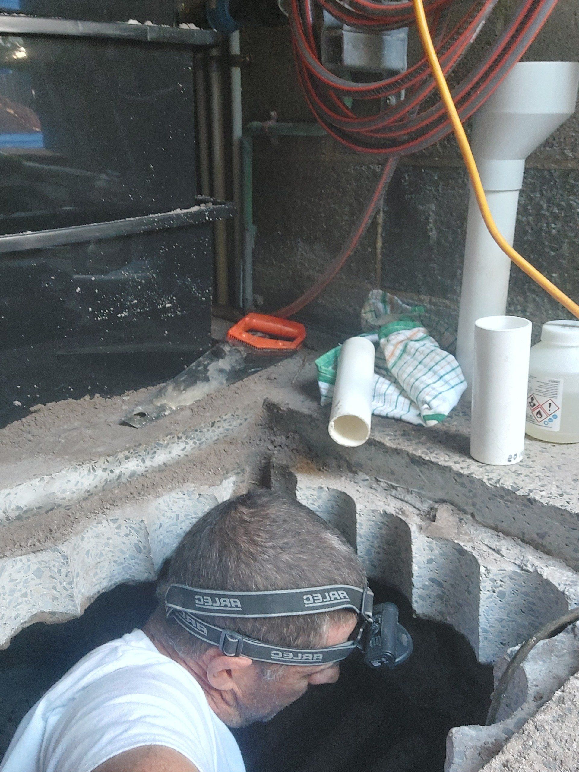 A man wearing a headlamp is looking into a hole in the ground.