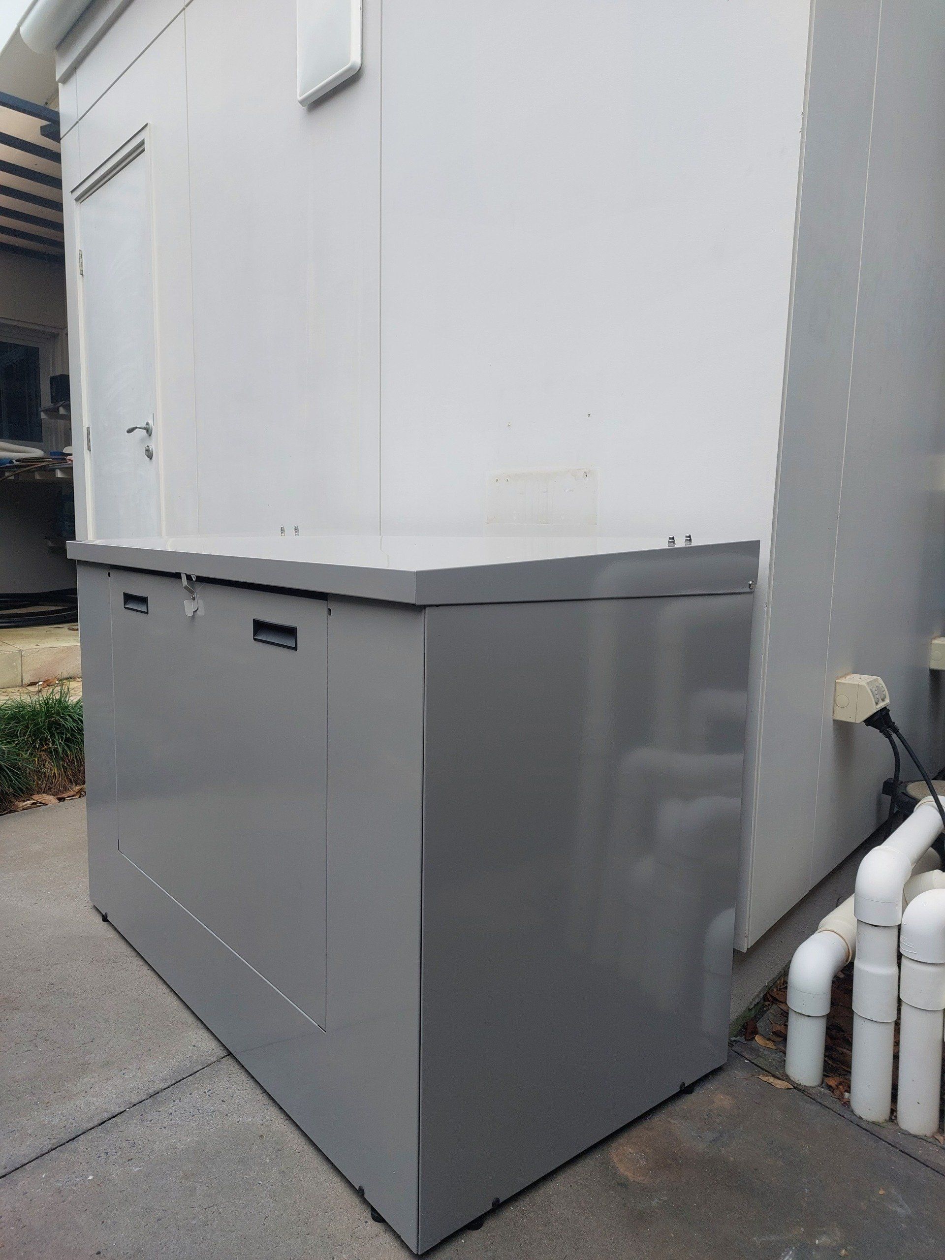 A large gray box is sitting next to a white building.