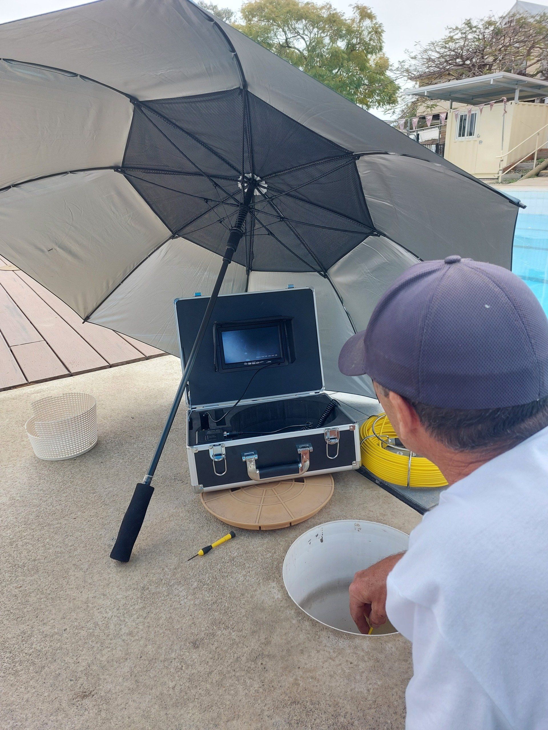 A man is looking at a camera in a case under an umbrella.