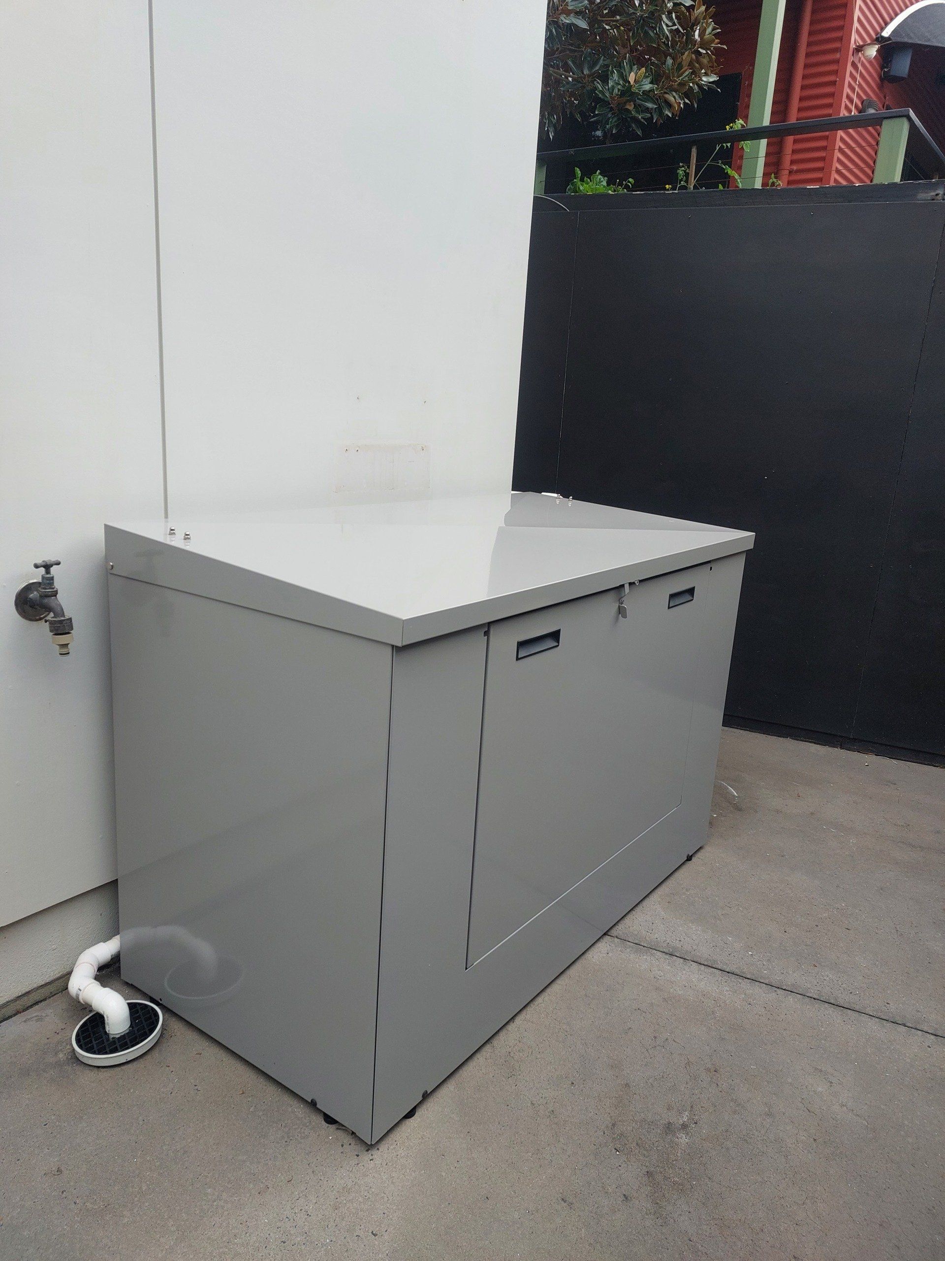 A gray box is sitting on a sidewalk next to a faucet.