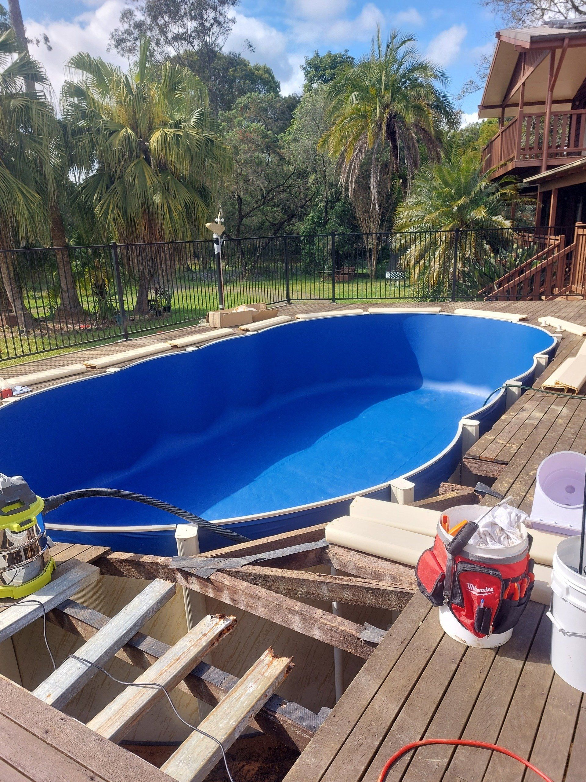 A large blue swimming pool is being built on a wooden deck.