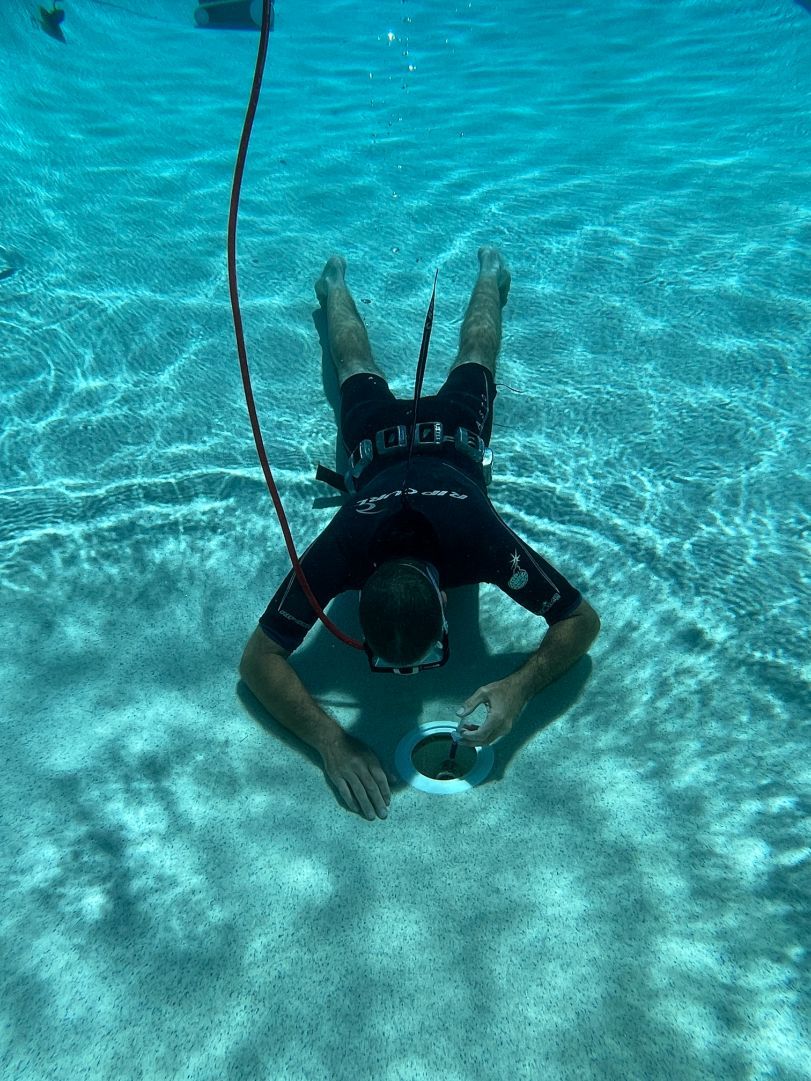 Man Fixing Drain Hole Under The Pool — Leak Detection & Swimming Pool Repairs in Ballina, NSW