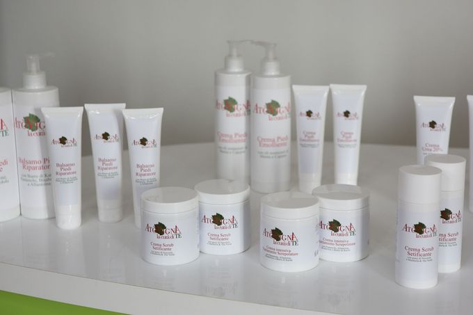 Una collezione di flaconi e vasetti bianchi per la cura della pelle, con etichette floreali abbinate, esposti su una superficie bianca.