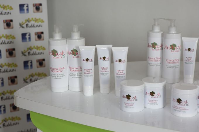 Una collezione di flaconi e vasetti di prodotti per la cura della pelle di marca, disposti su un bancone bianco, con uno sfondo che raffigura i loghi.