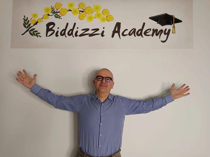 Una persona è in piedi con le braccia spalancate davanti a una parete bianca su cui campeggia l'insegna 