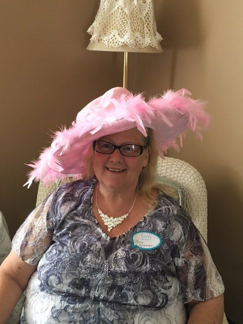 A woman wearing a pink hat and glasses is sitting in a chair.