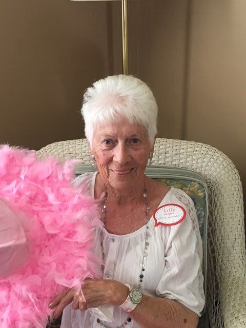 An elderly woman is sitting in a chair holding a pink boa.