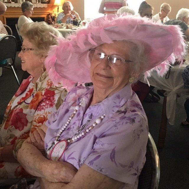A woman wearing a pink hat and glasses sits with her arms crossed