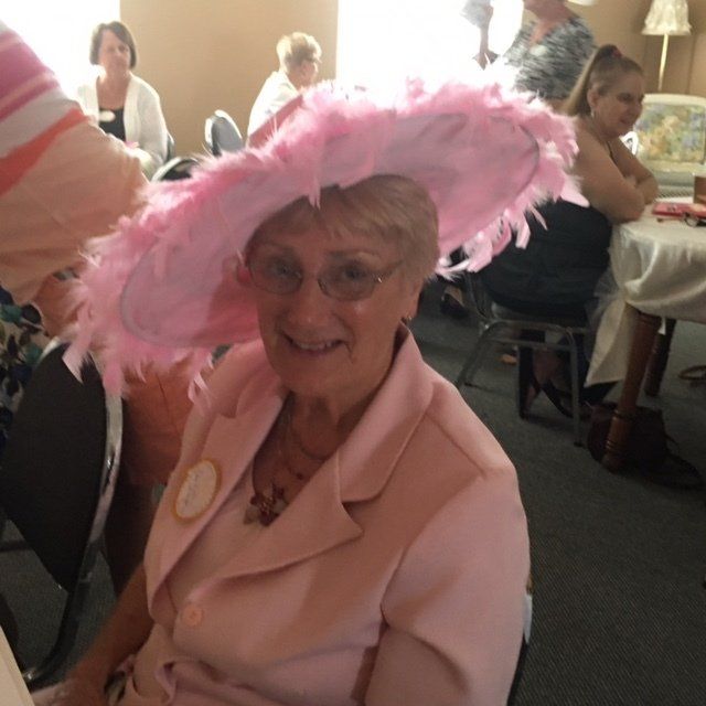 A woman wearing a pink hat and glasses sits at a table
