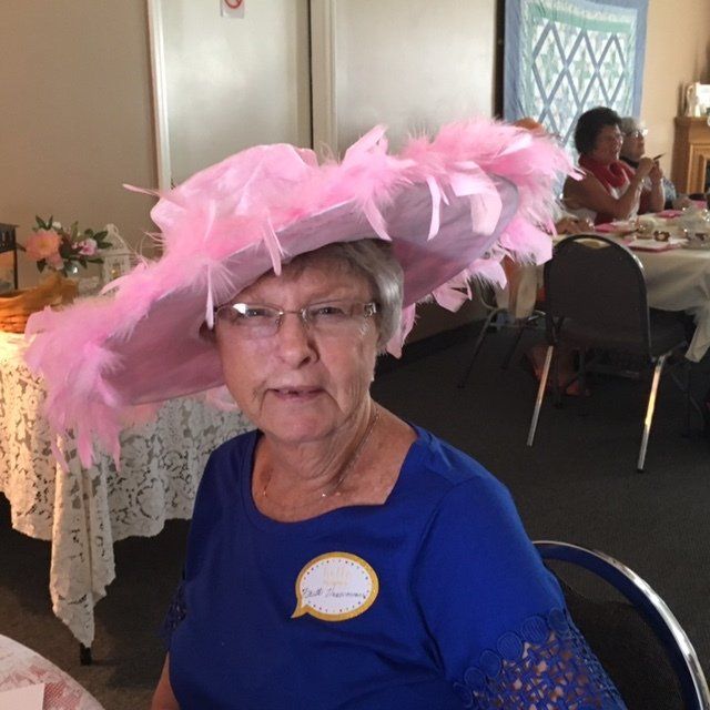 A woman wearing a large pink hat is sitting at a table