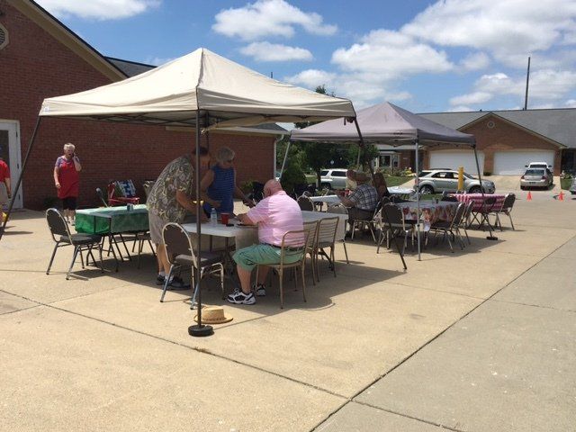 A group of people sitting at tables under tents in a driveway