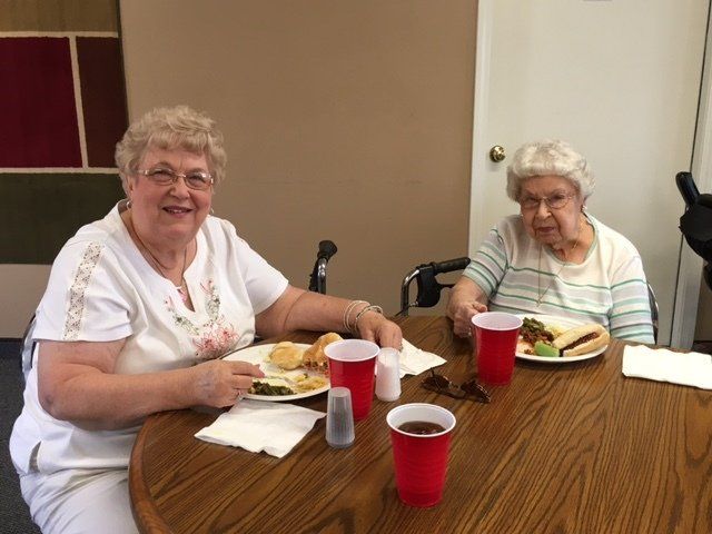 Two elderly women are sitting at a table with plates of food and red cups