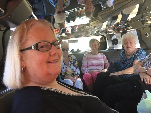 A woman wearing glasses is sitting in the back seat of a car with other people.