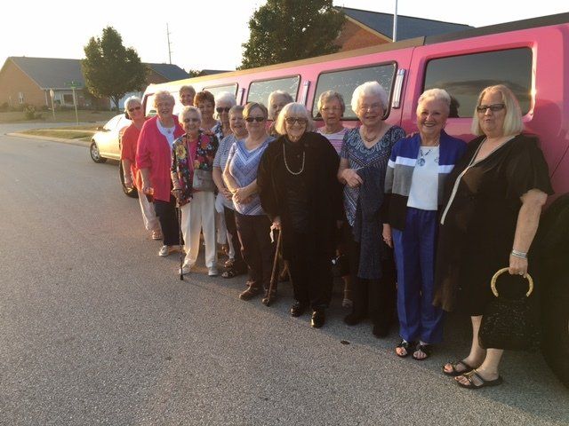 A group of women standing in front of a pink limousine