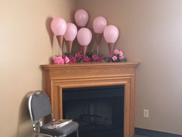 A chair sits in front of a fireplace decorated with pink balloons and flowers