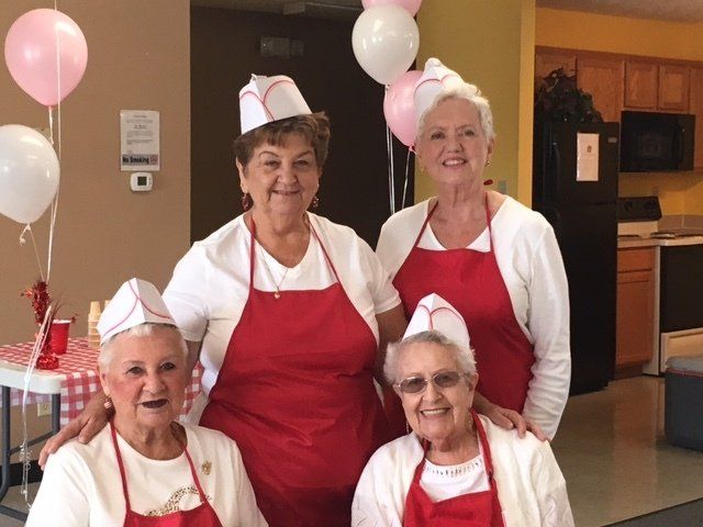Four older women wearing red aprons and hats pose for a picture