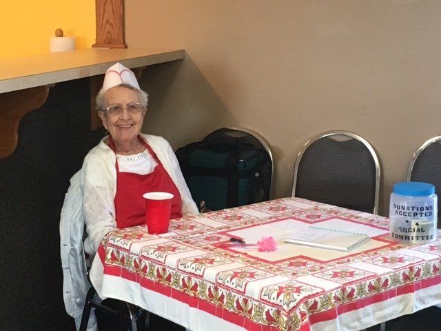 An elderly woman sits at a table with a red cup