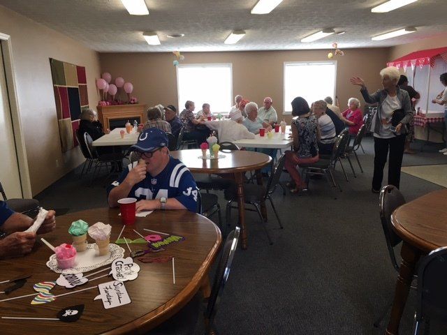 A group of people are sitting at tables in a room and one man is wearing a jersey with the number 24 on it