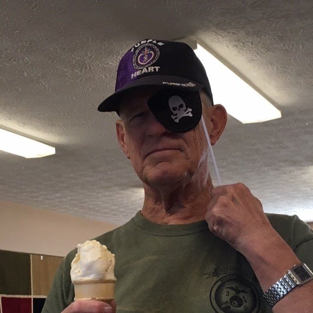 A man wearing a purple heart hat is holding an ice cream cone