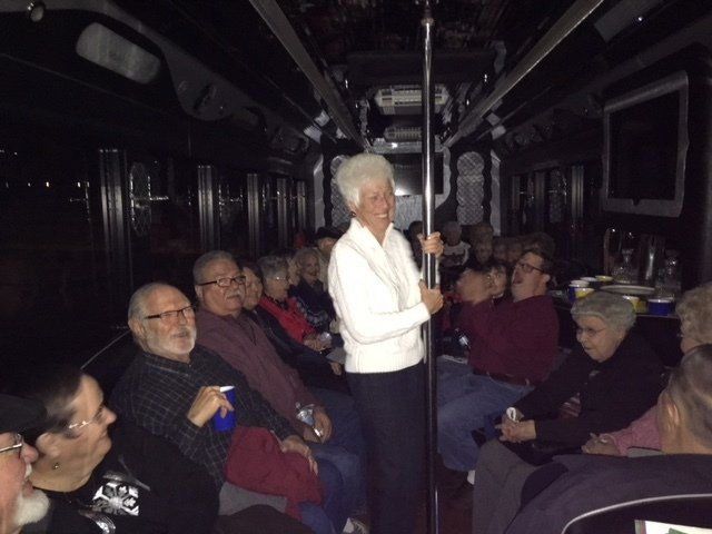 A group of people sitting on a bus with a woman standing in the middle