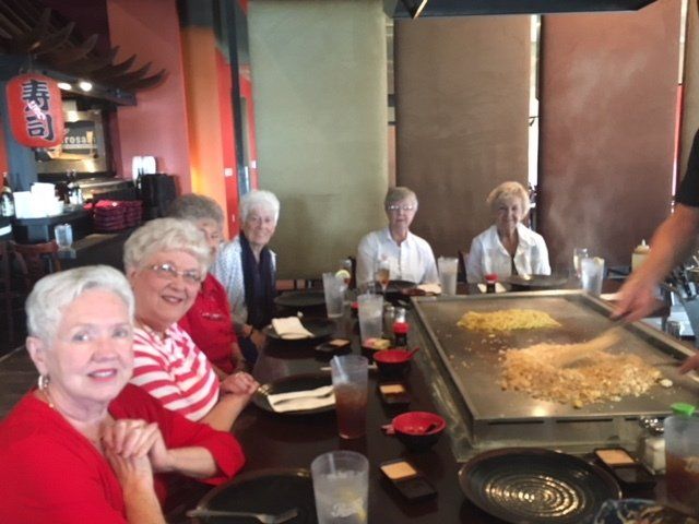 A group of older women are sitting at a table in front of a grill