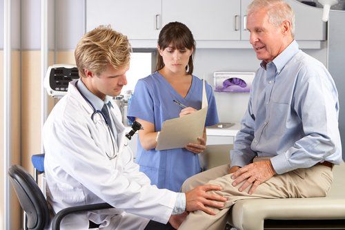 A doctor is examining a patient 's knee while a nurse looks on.