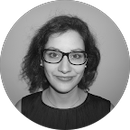 A woman wearing glasses and earrings is smiling in a black and white photo.