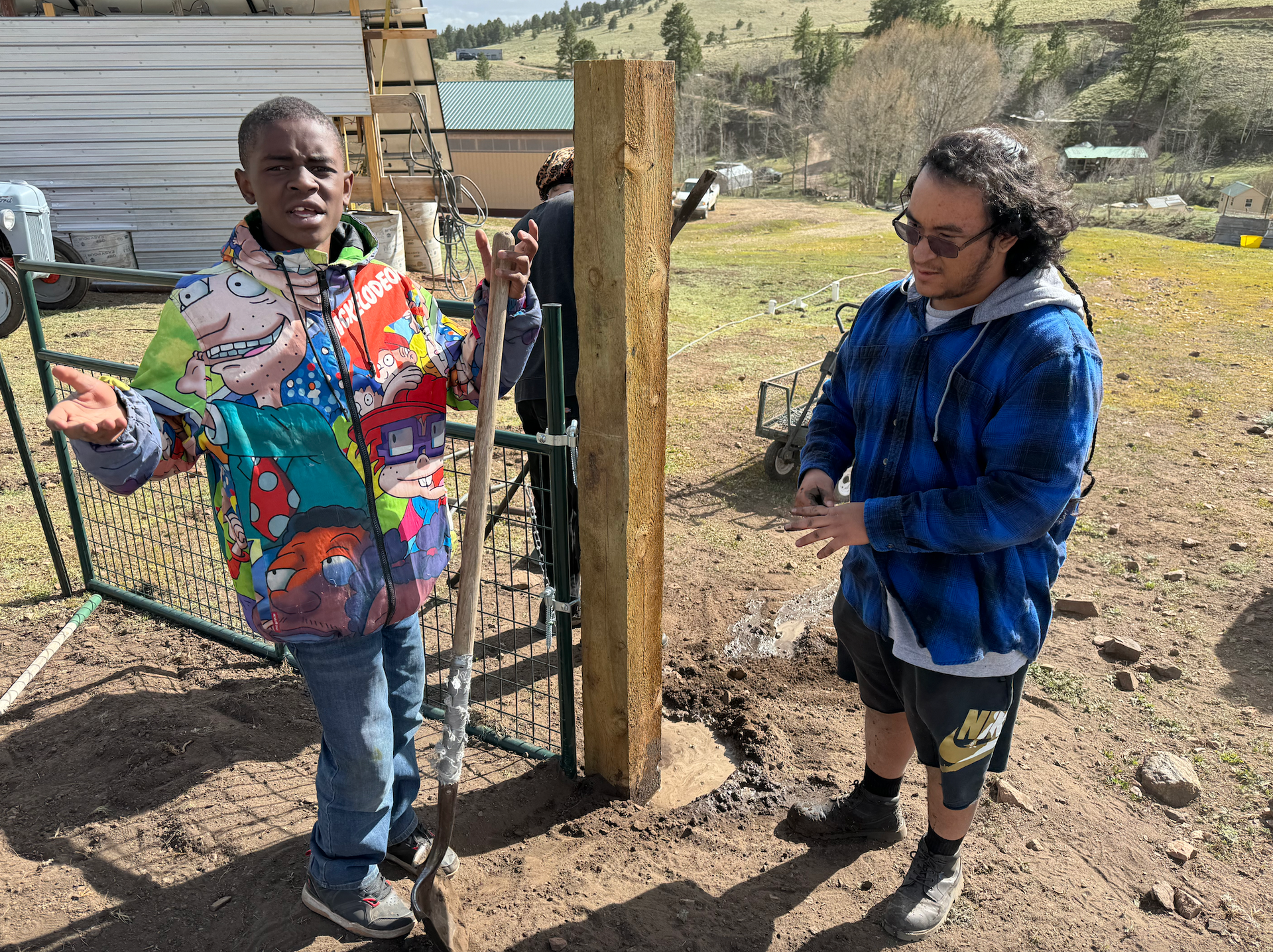 A boy in a colorful jacket is standing next to a man holding a shovel.