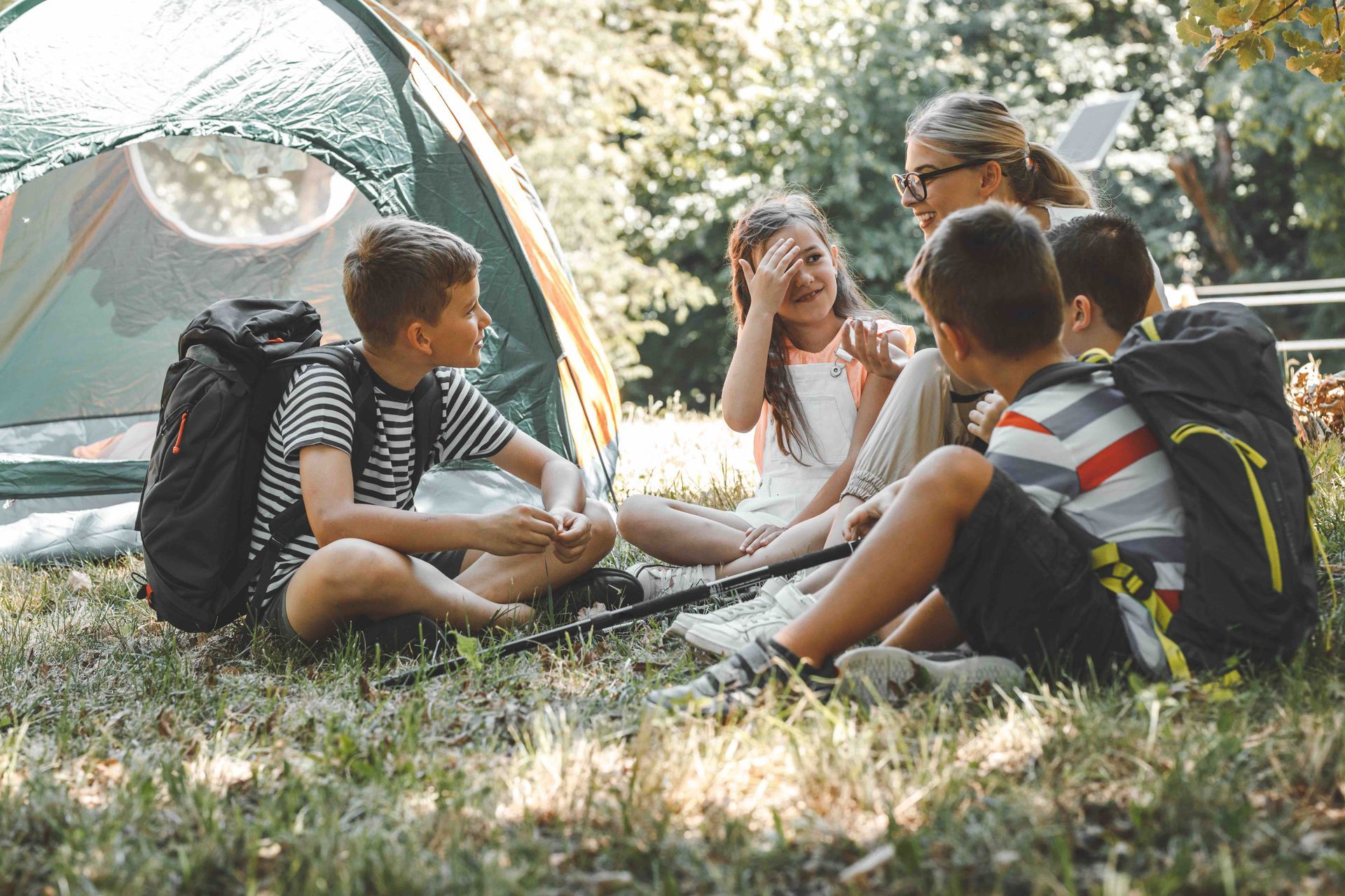 A group of children are sitting in a circle in front of a tent.