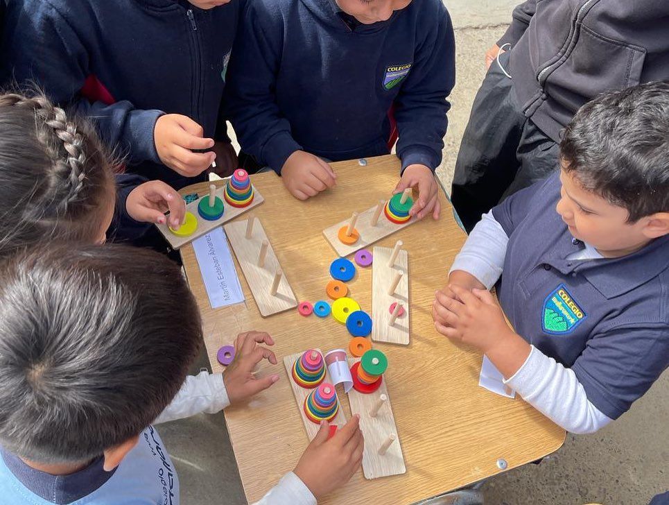 Niños sentados a una mesa, jugando a un juego de apilar aros de madera de colores.