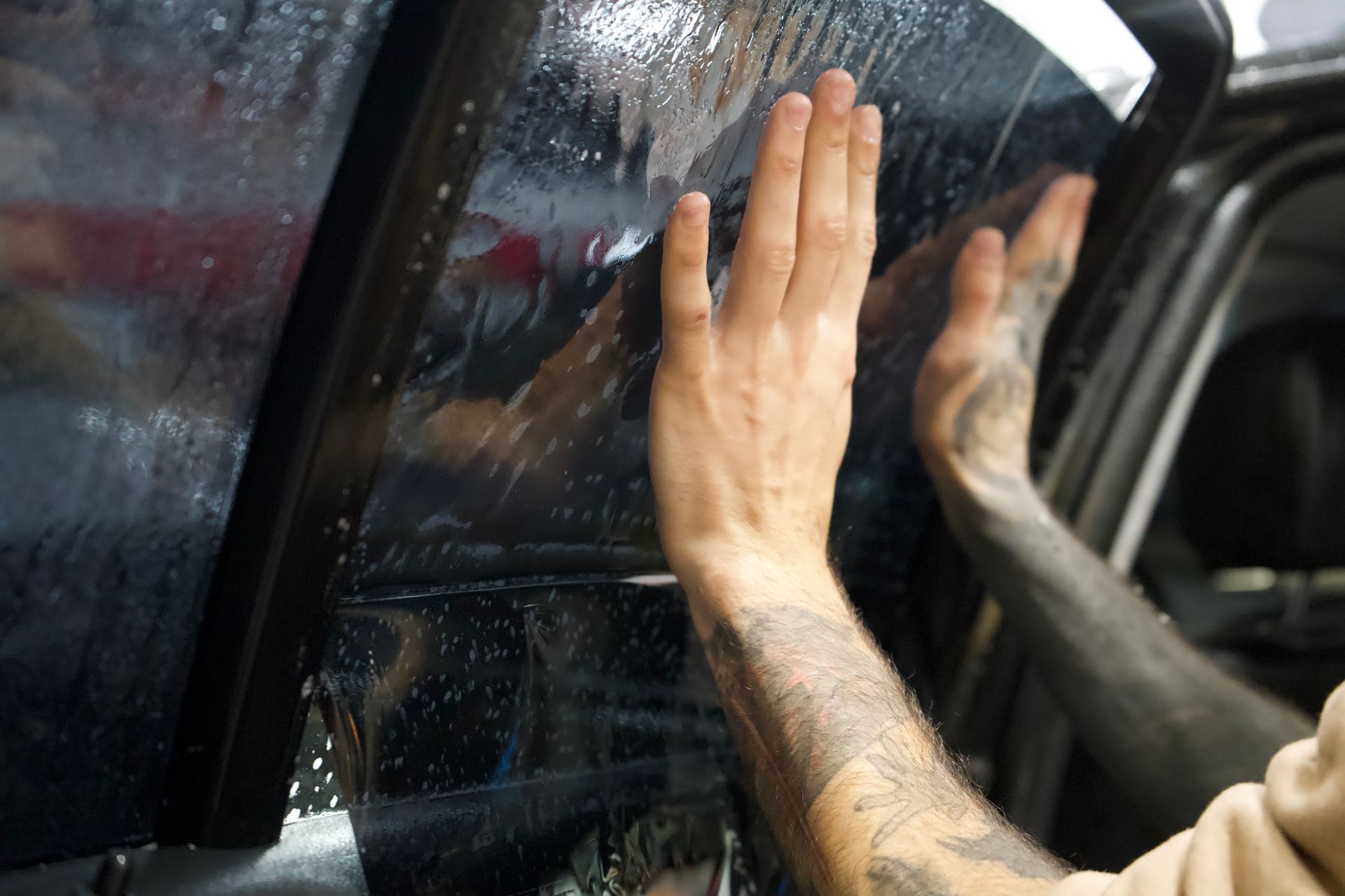 Hands smoothing tinted film onto a car window.
