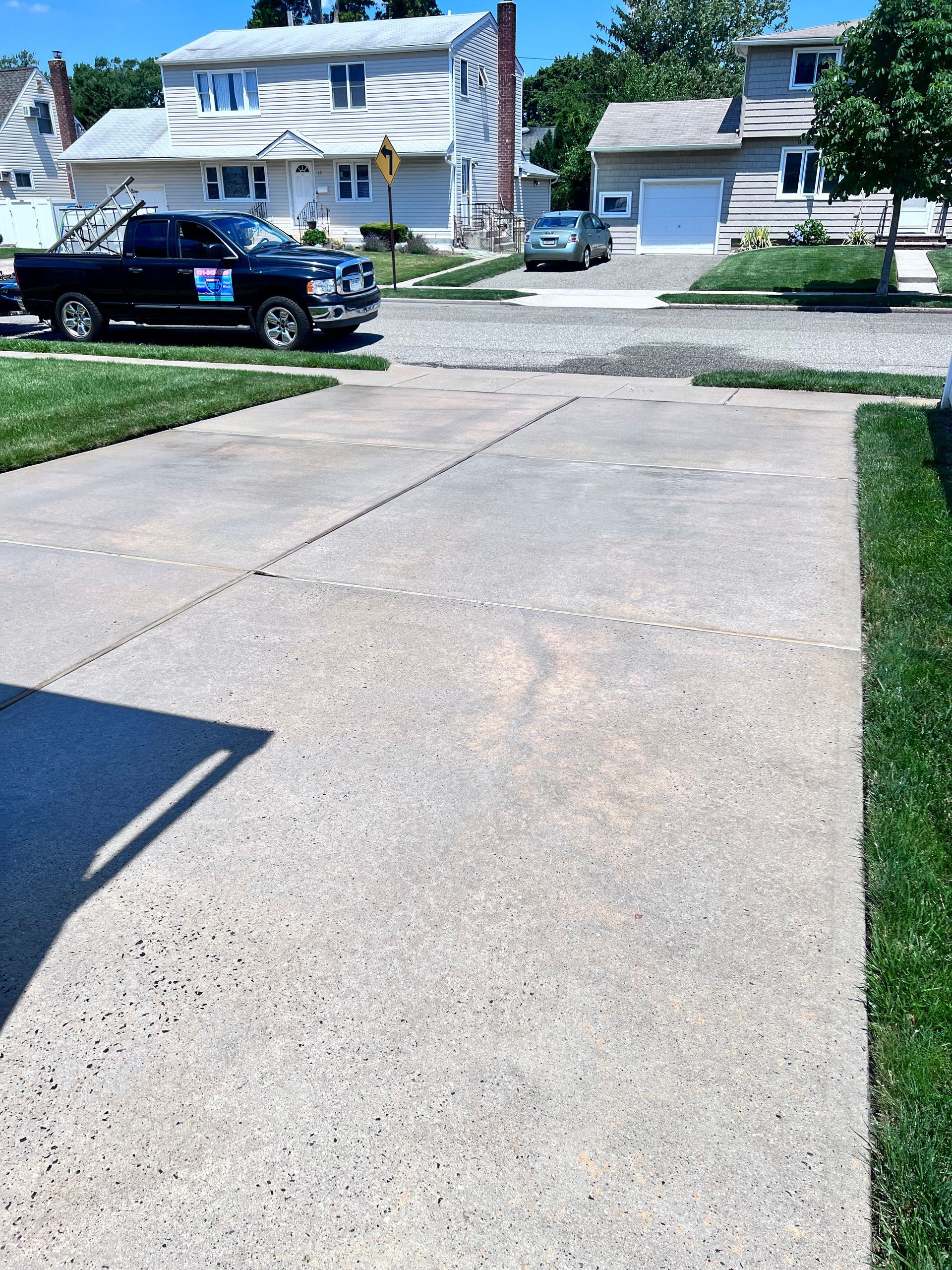 A gray concrete driveway with a black truck parked on the left, leading to a residential street with houses.