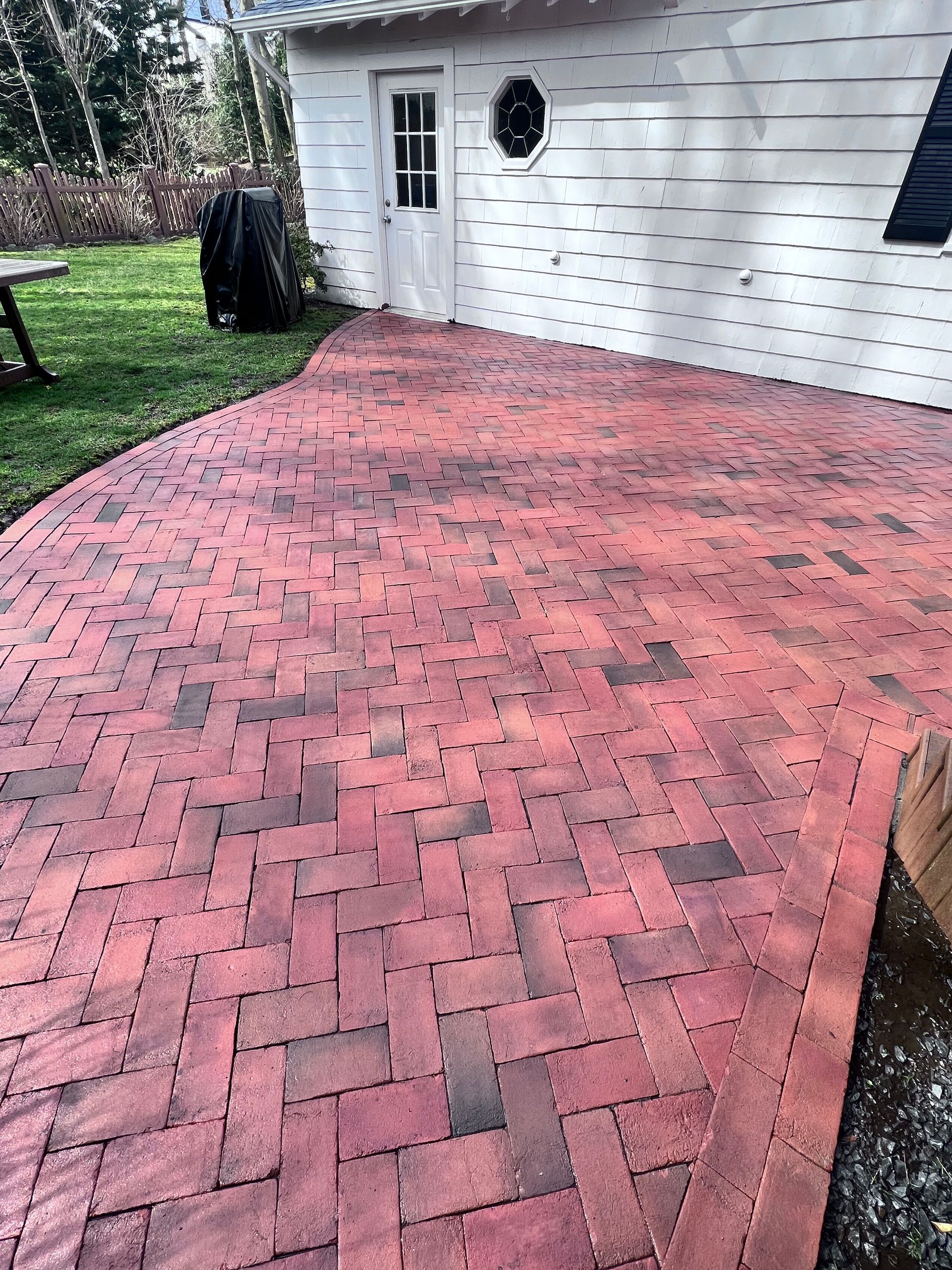 Red brick patio with a herringbone pattern outside a white building with a small door.