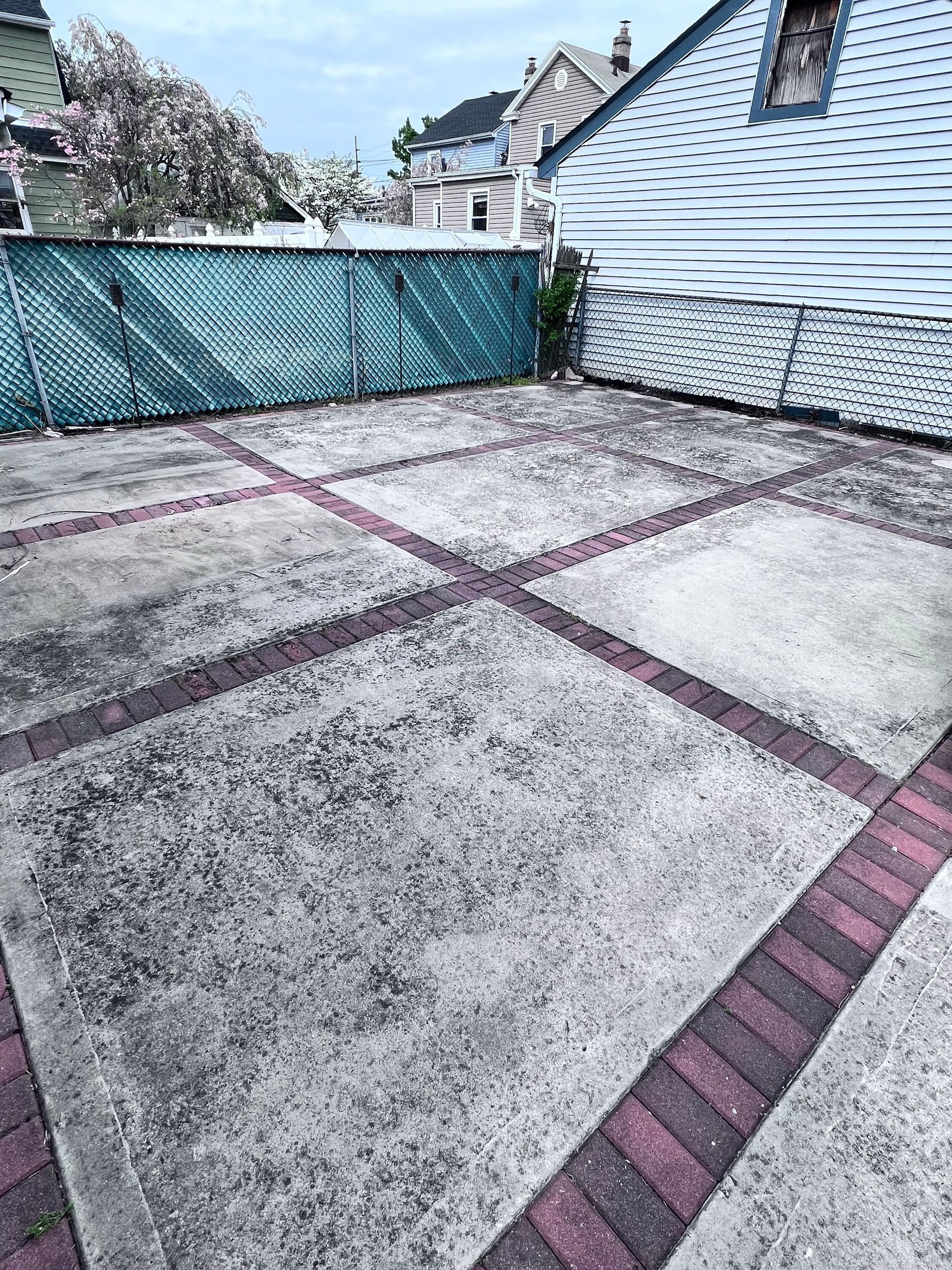 Concrete patio with red brick borders, blue fence, and blue-sided house in the background.