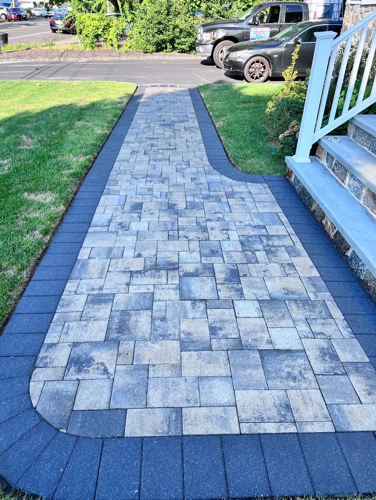 Brick walkway leading from the street to a house. The path is bordered by black bricks, with gray and tan pavers in the center.