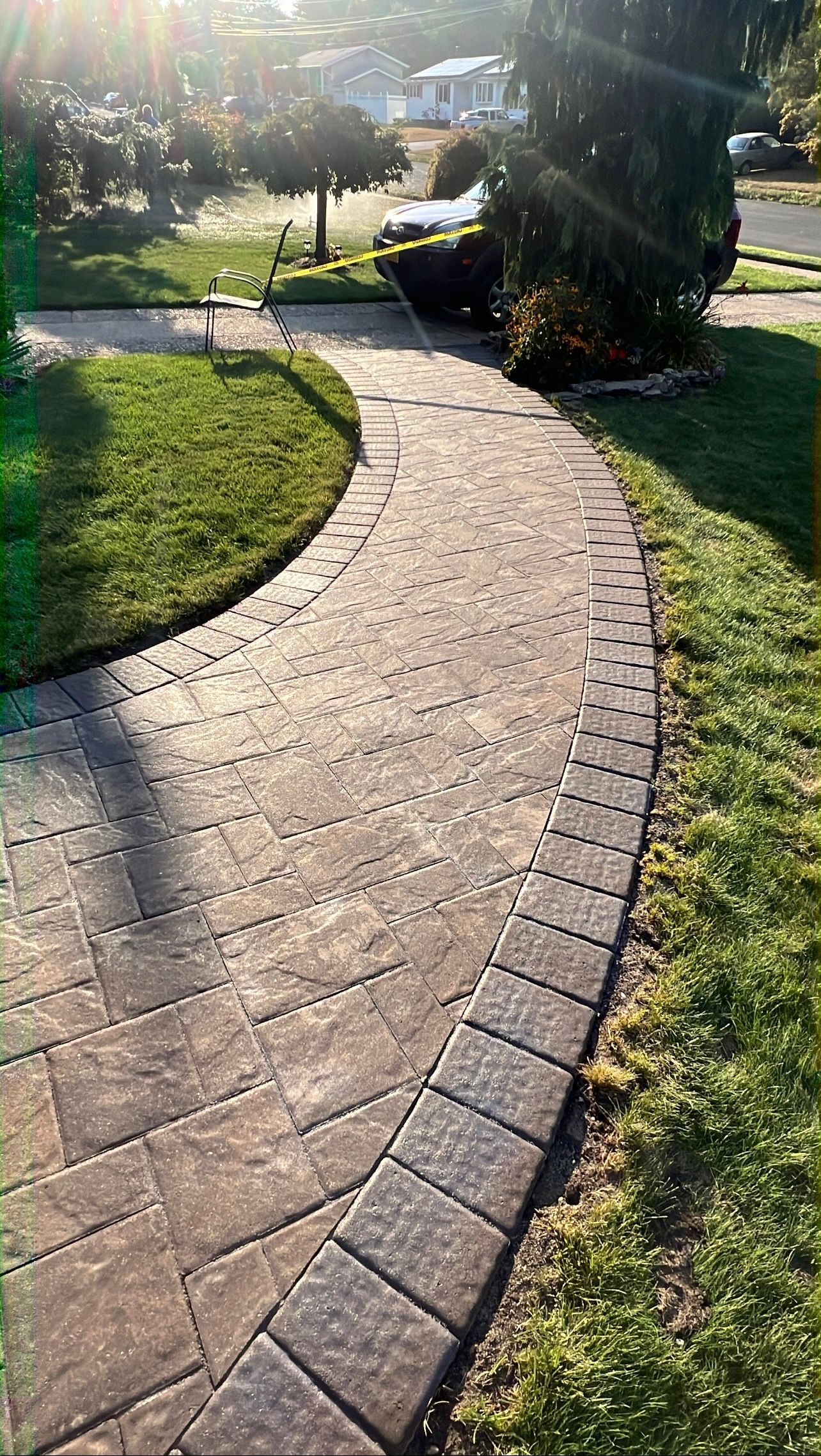 Brick pathway curves through green grass towards a home; bright sunlight.