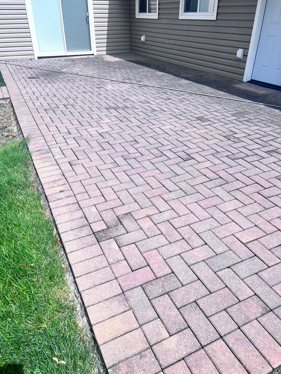 Brick patio with a herringbone pattern, adjacent to a building with siding and sliding glass door.