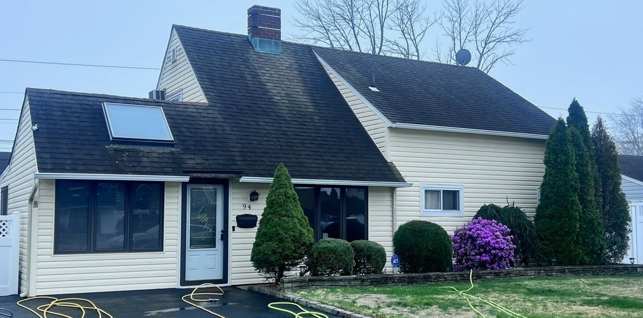 A beige suburban house with a dark roof, chimney, and front door. Landscaping includes bushes and a tree.