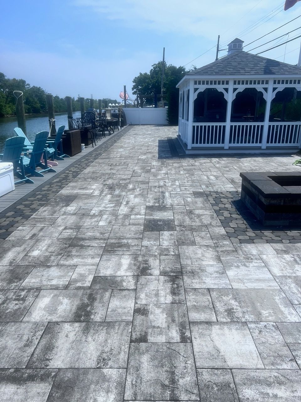Paver patio with gazebo, fire pit, and water views. Several Adirondack chairs sit by the water.