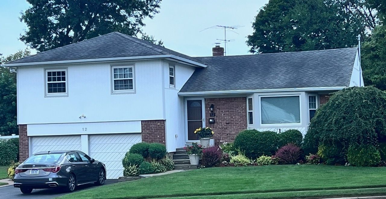 A two-story white house with a brick facade, two-car garage, and a car parked in the driveway on a green lawn.