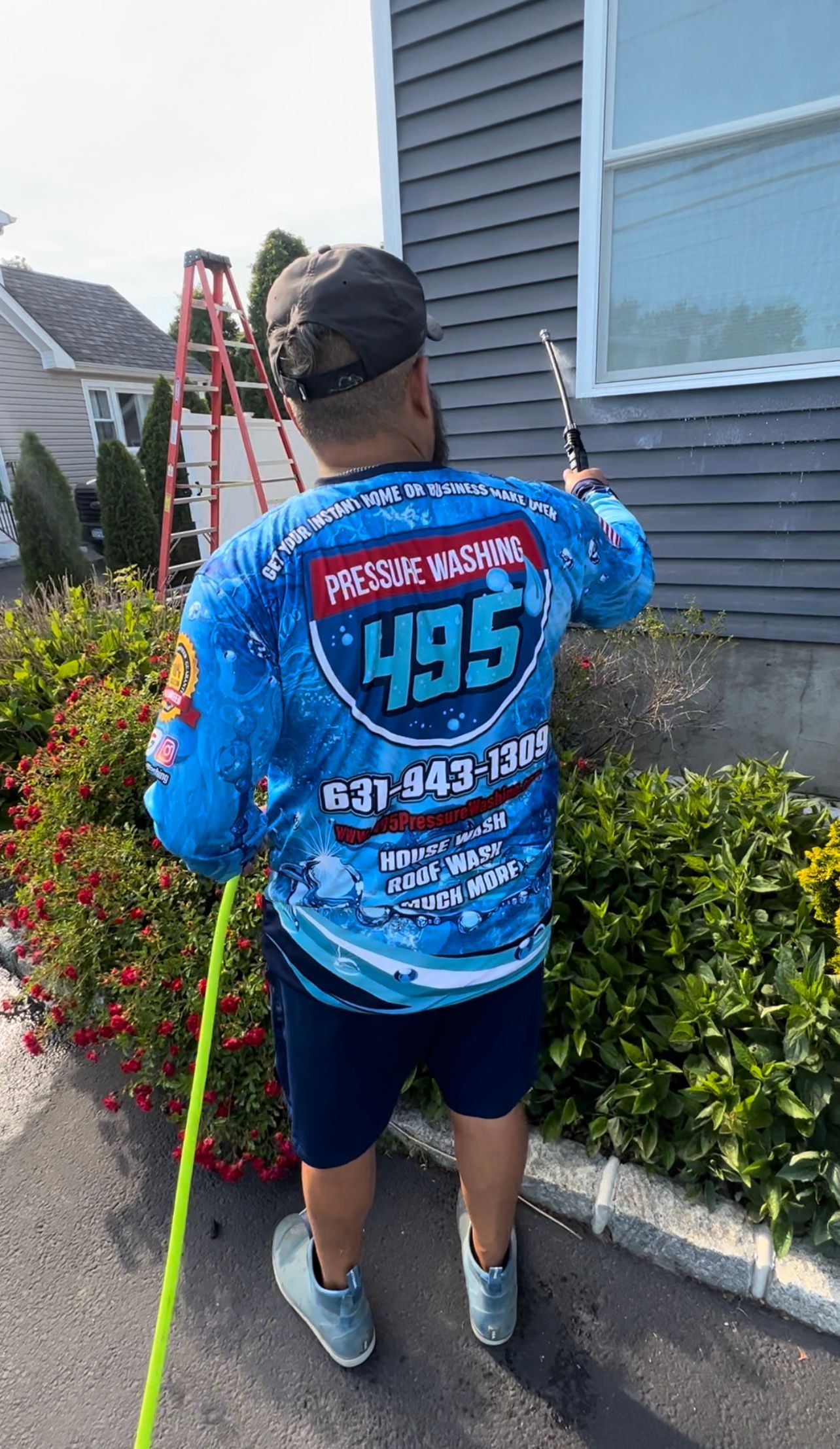Man power washing a house, wearing a blue long-sleeved shirt with 