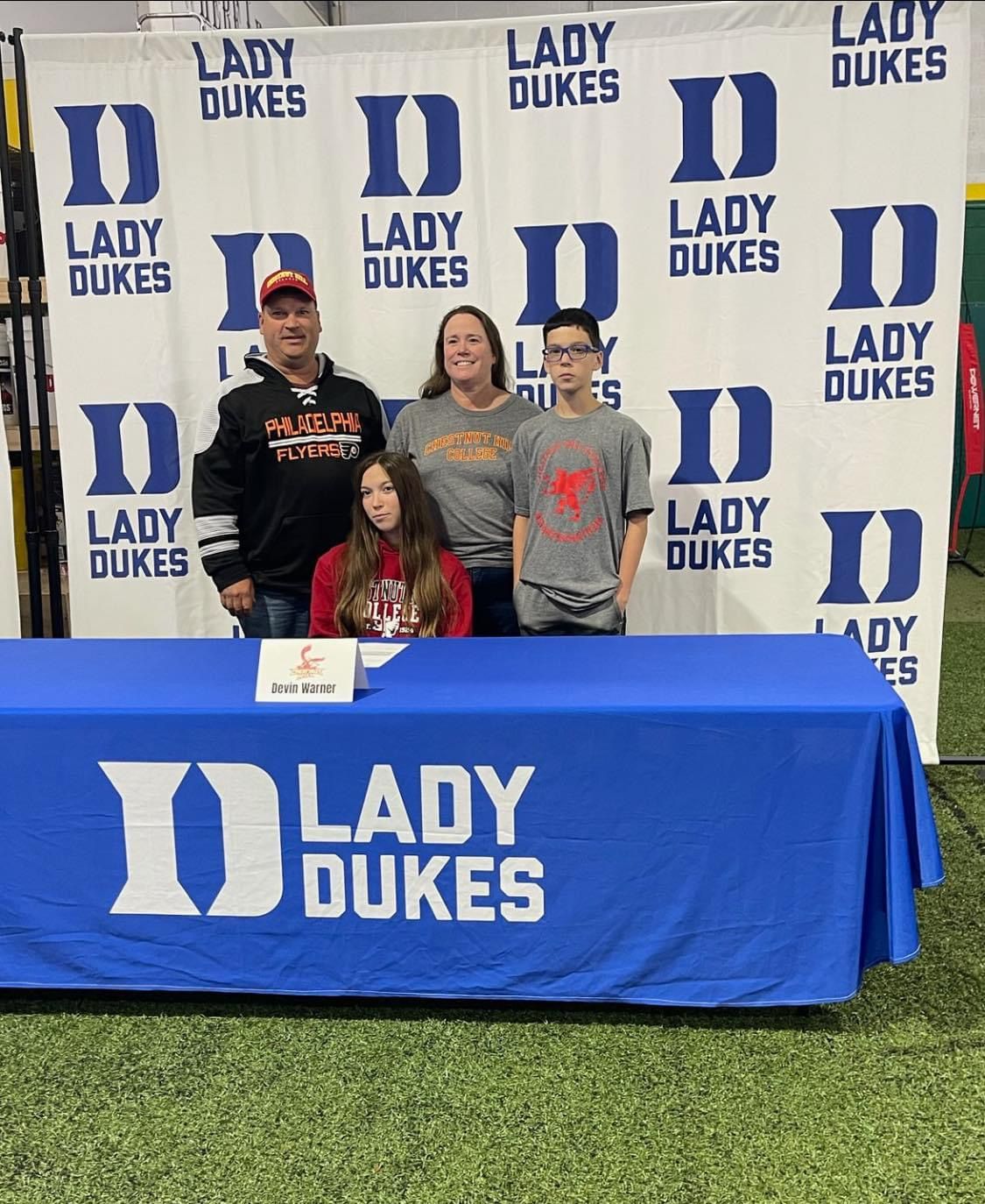 A group of people standing around a table with a Lady Dukes banner behind them — Elkton, MD — Maryland Legends Baseball