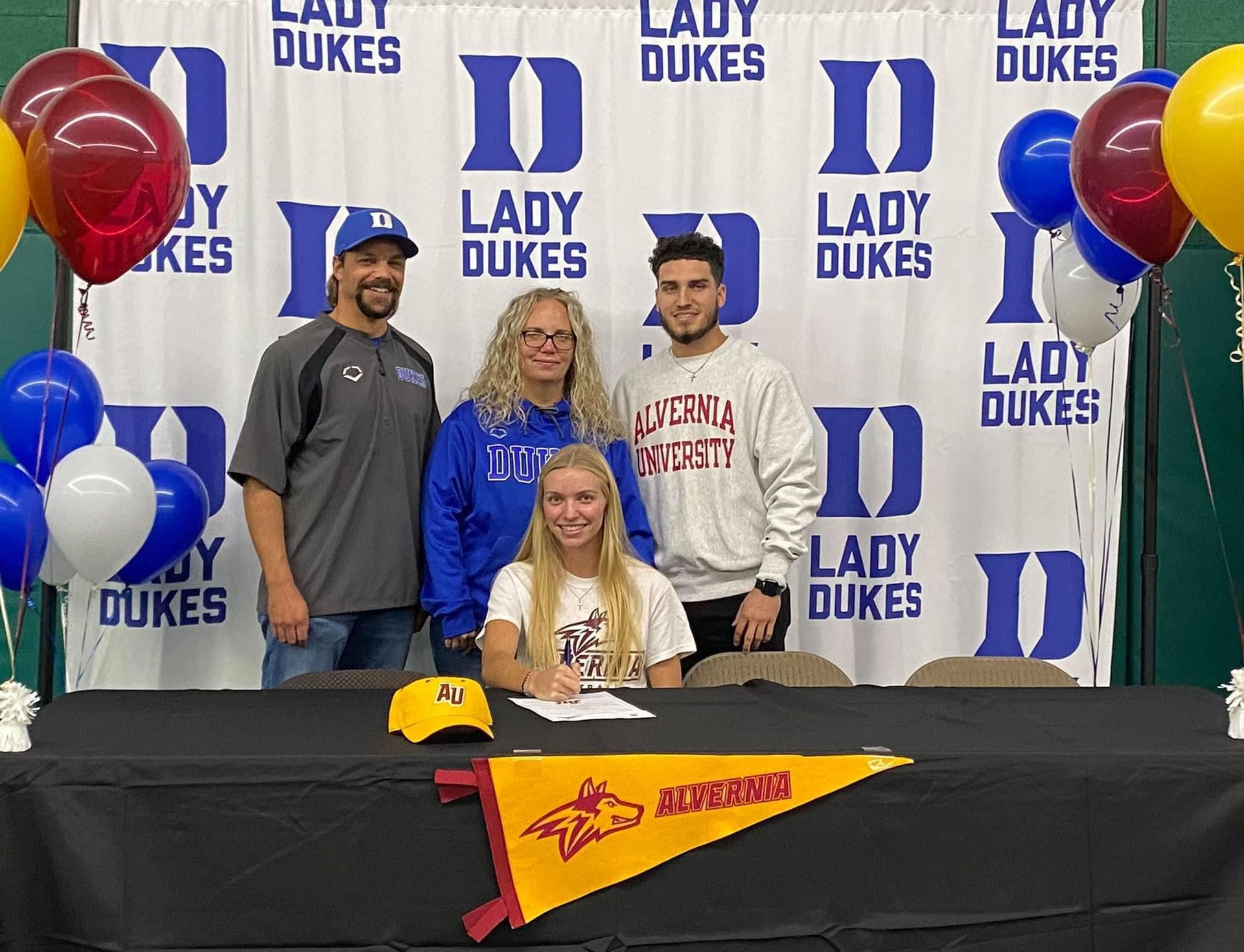 Four persons standing around a table in front of a Lady Dukes banner — Elkton, MD — Maryland Legends Baseball