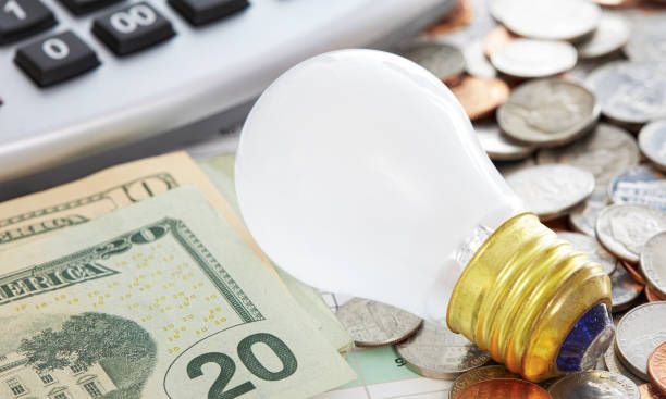 A Light Bulb is Sitting on Top of a Pile of Money Next to a Calculator | Great Bend, KS | P&S Electric