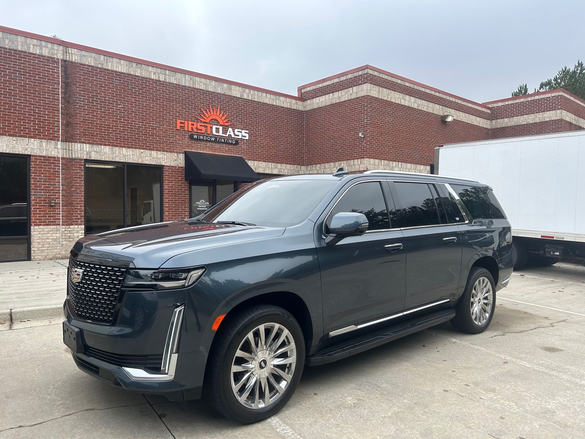 A black cadillac escalade is parked in front of a brick building.