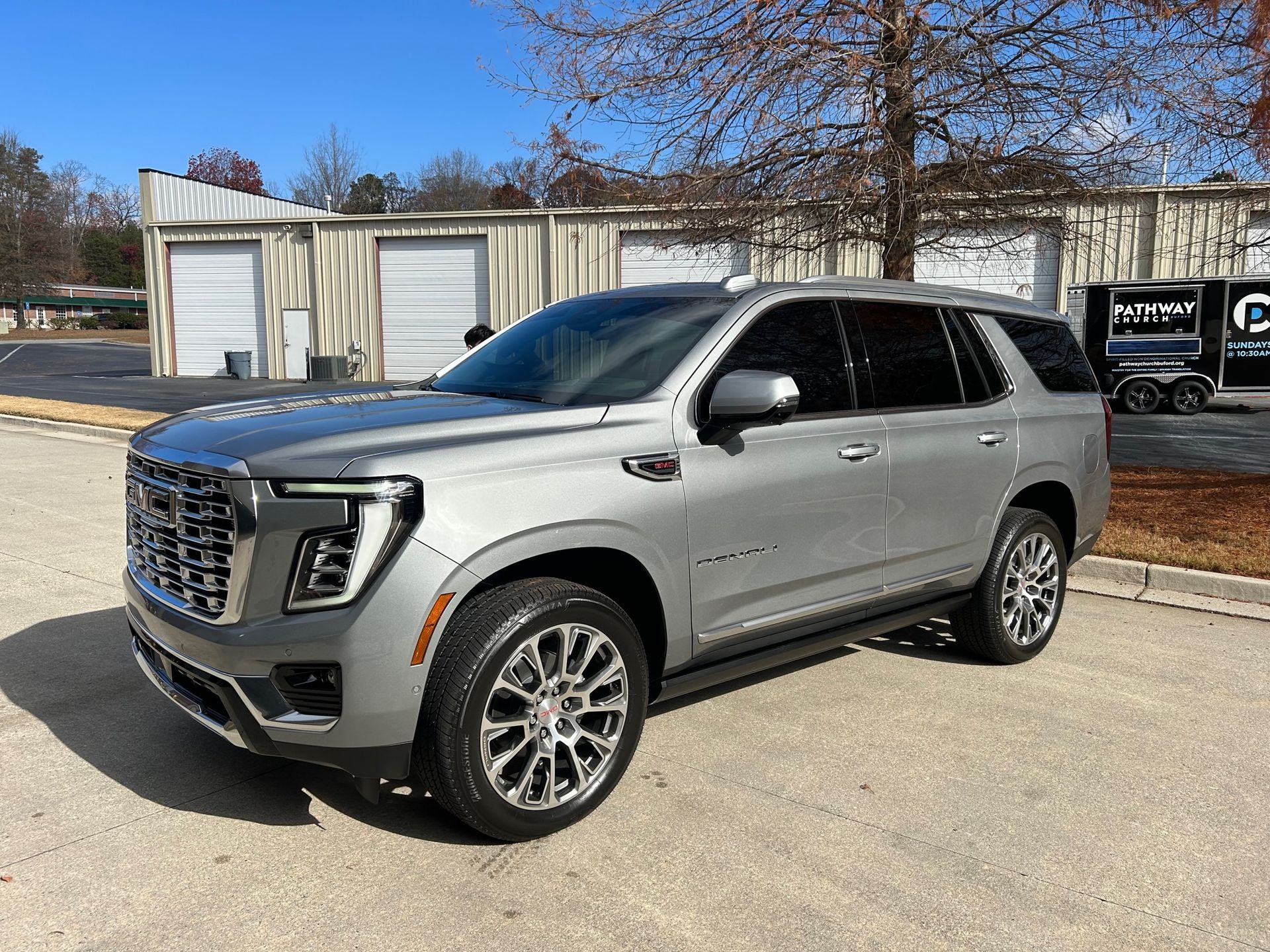 A silver gmc yukon is parked in a parking lot in front of a building.