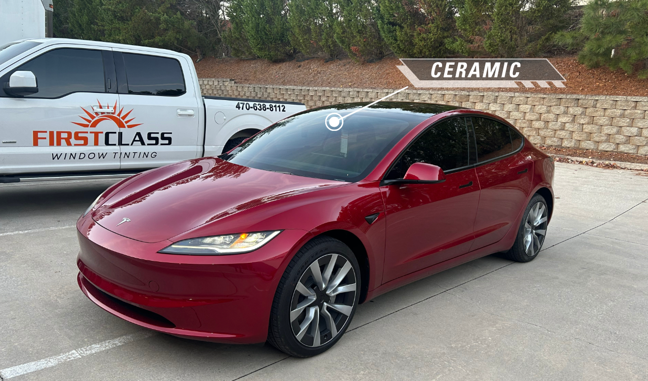 A red tesla model 3 is parked in a parking lot next to a white truck.
