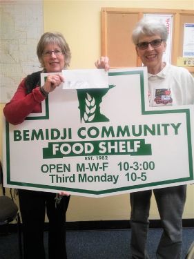 Two women holding a sign for the bemidji community food shelf