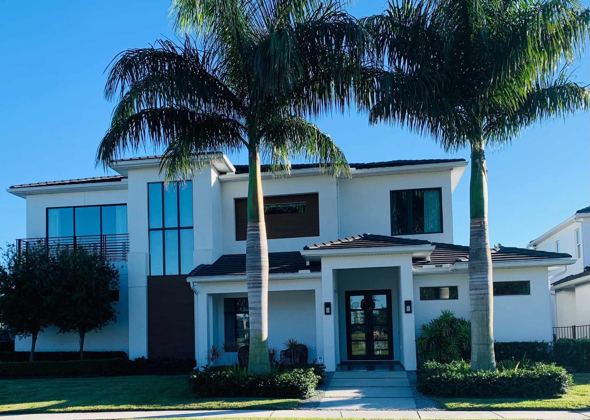 Two-story modern home with white exterior, dark windows, and palm trees in front.
