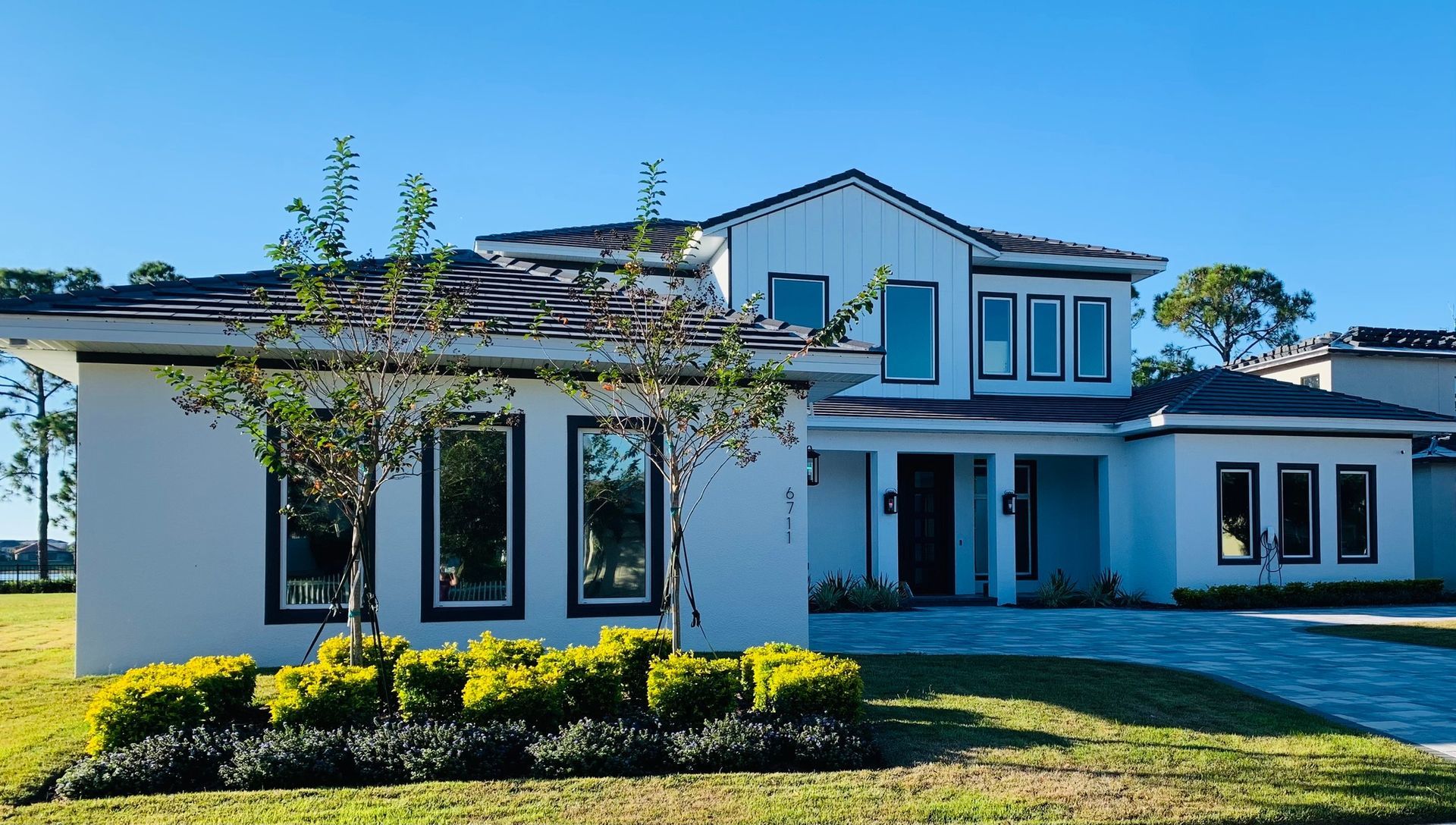 White two-story house with dark trim and roof, bright blue sky, and green lawn.
